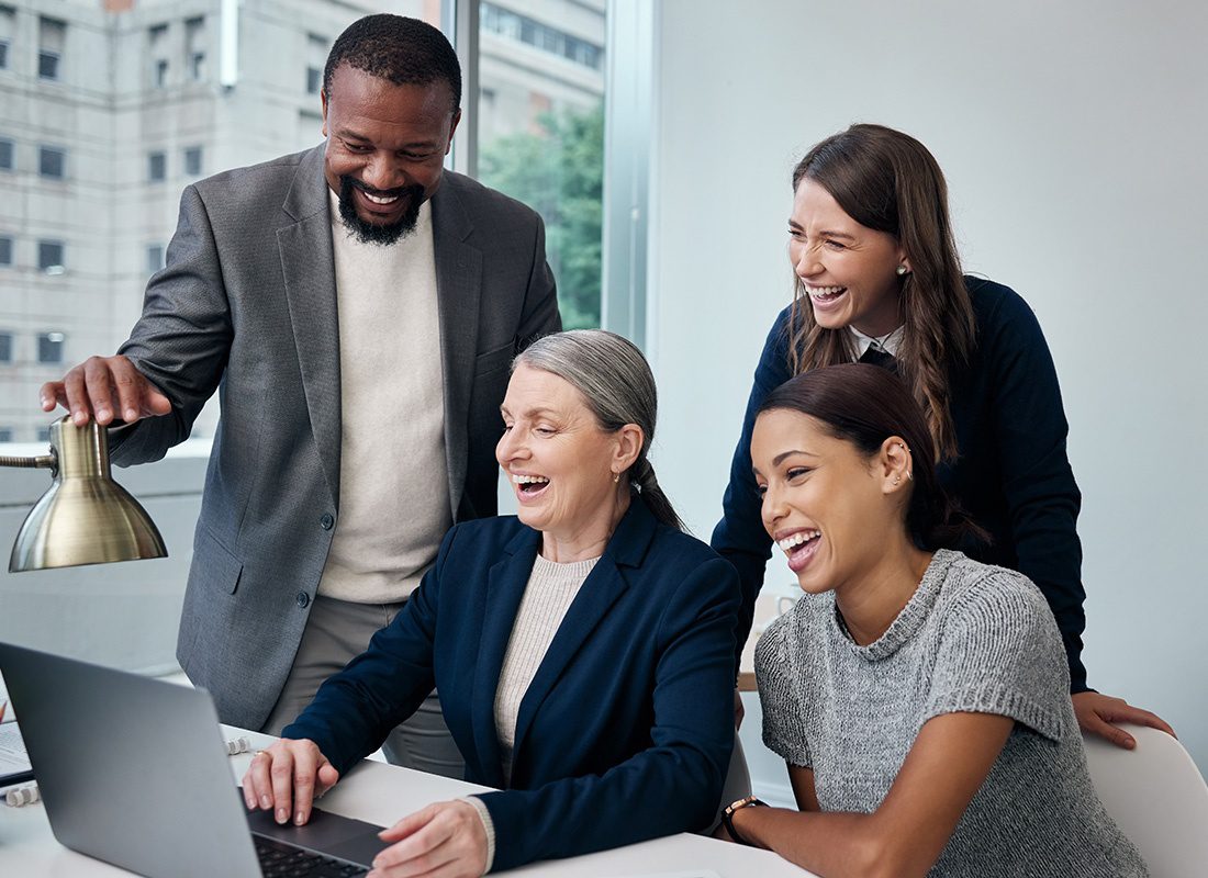 Employee Benefits - Portrait of a Small Group of Diverse Cheerful Employees Working on a Laptop Together in the Office