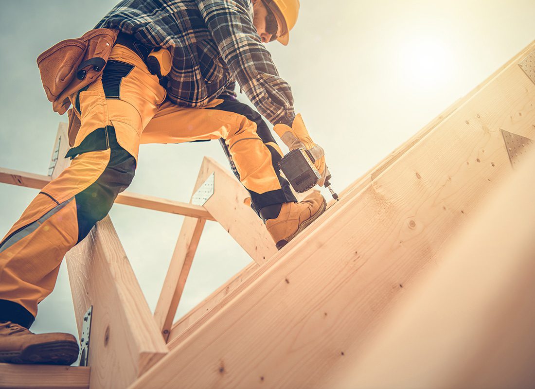 Insurance by Industry - View of a Contractor Holding a Drill While Working on a Roof Frame on a New House Build Project