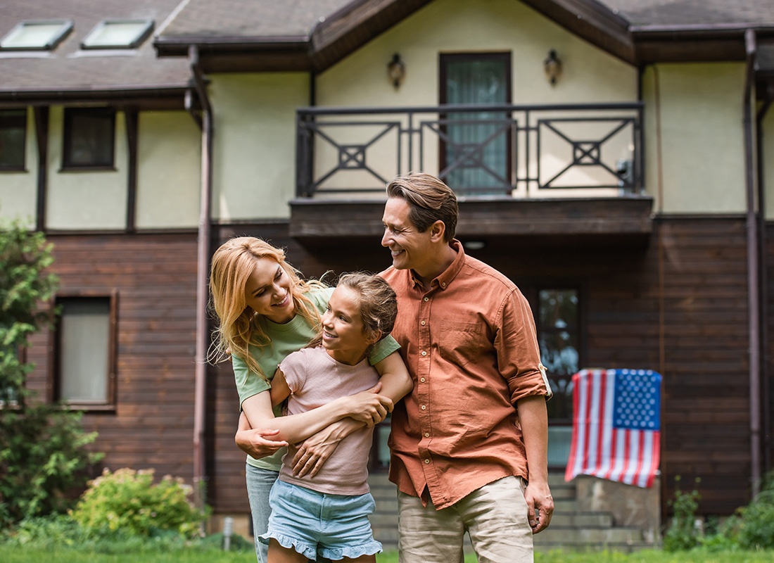 Personal Insurance - Portrait of a Family with a Daughter Having Fun Standing Outside Their Home with an American Flag on the Front Steps on a Sunny Day